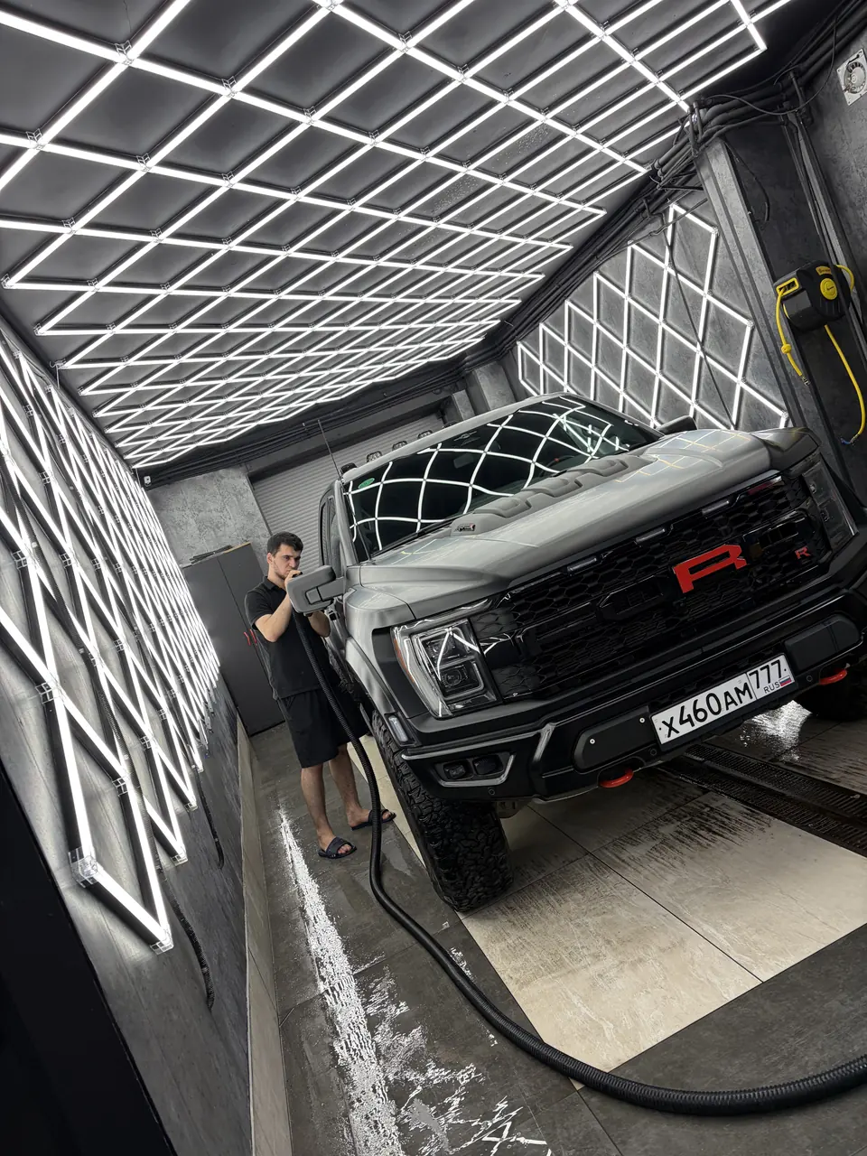 Мастер обрабатывает серый пикап Ford F-150 Raptor в моечном боксе