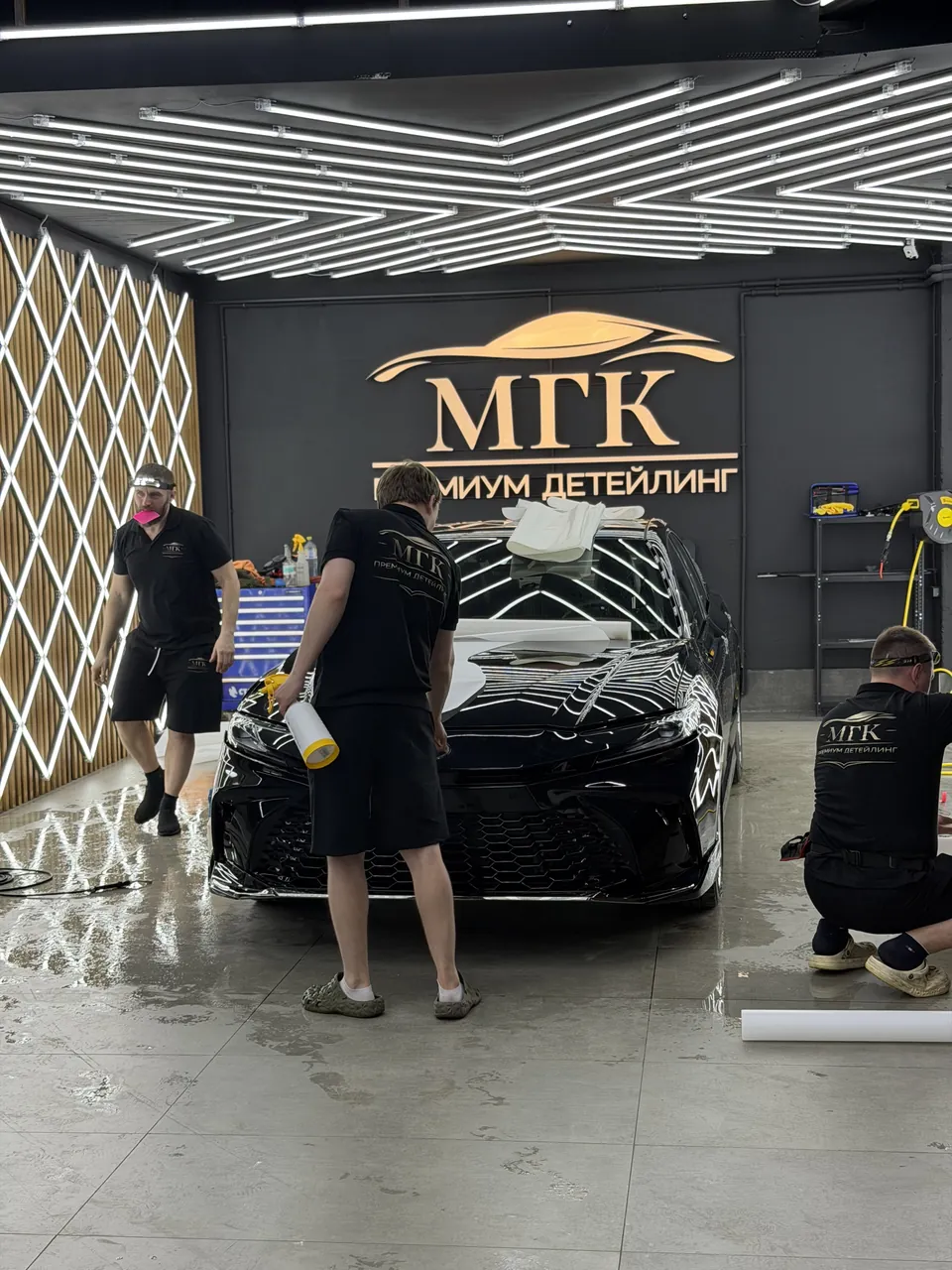 Три мастера МГК устанавливают защитную плёнку на чёрный автомобиль
