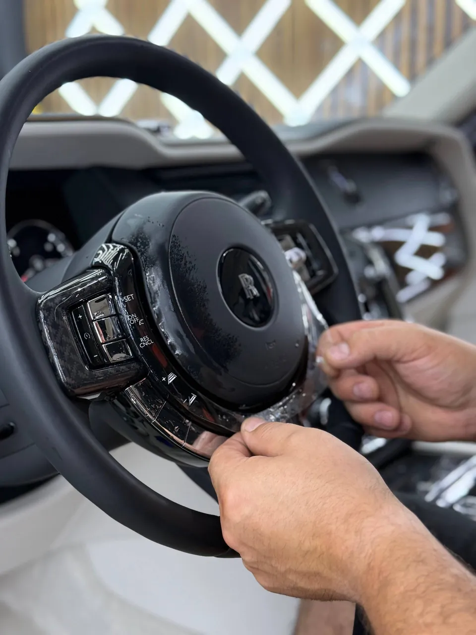 Мастер оклеивает защитной плёнкой глянцевые элементы рулевого колеса Rolls-Royce